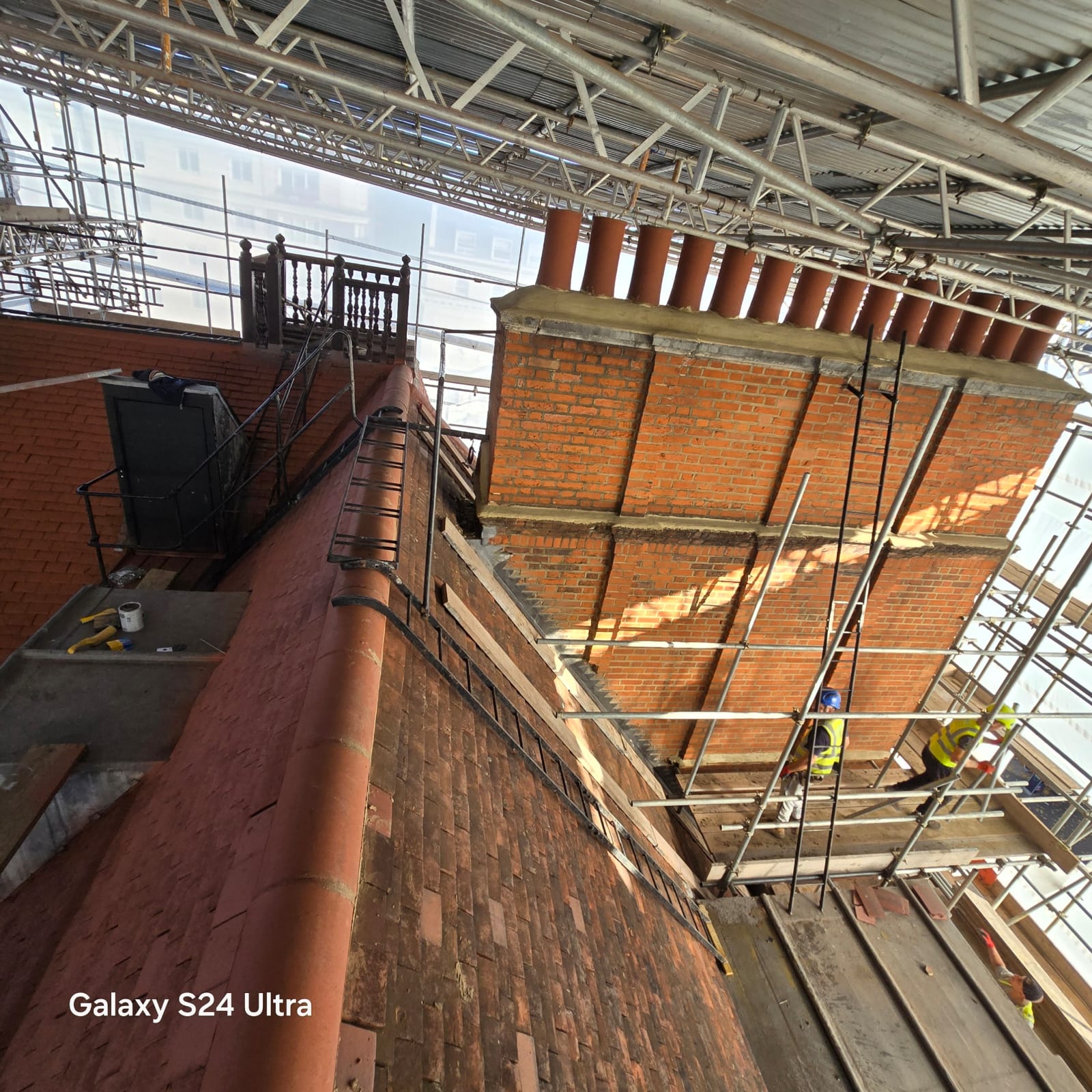 Original clay tiled slope, brick parapet and chimney pots seen from the scaffold before renewal