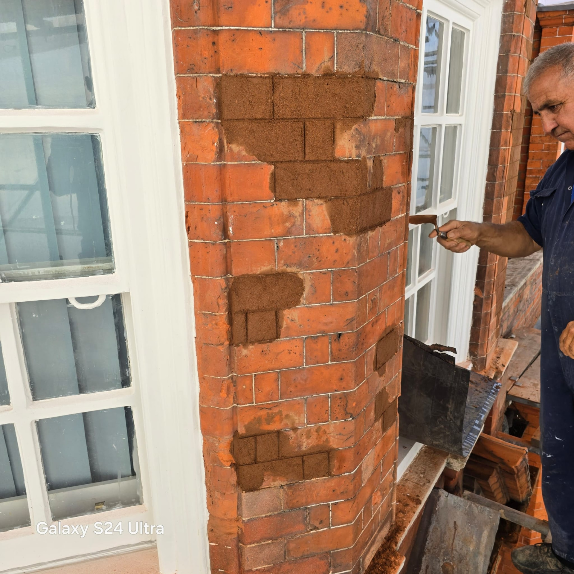 Bricklayer repointing and repairing the original brick pier beside a sash window