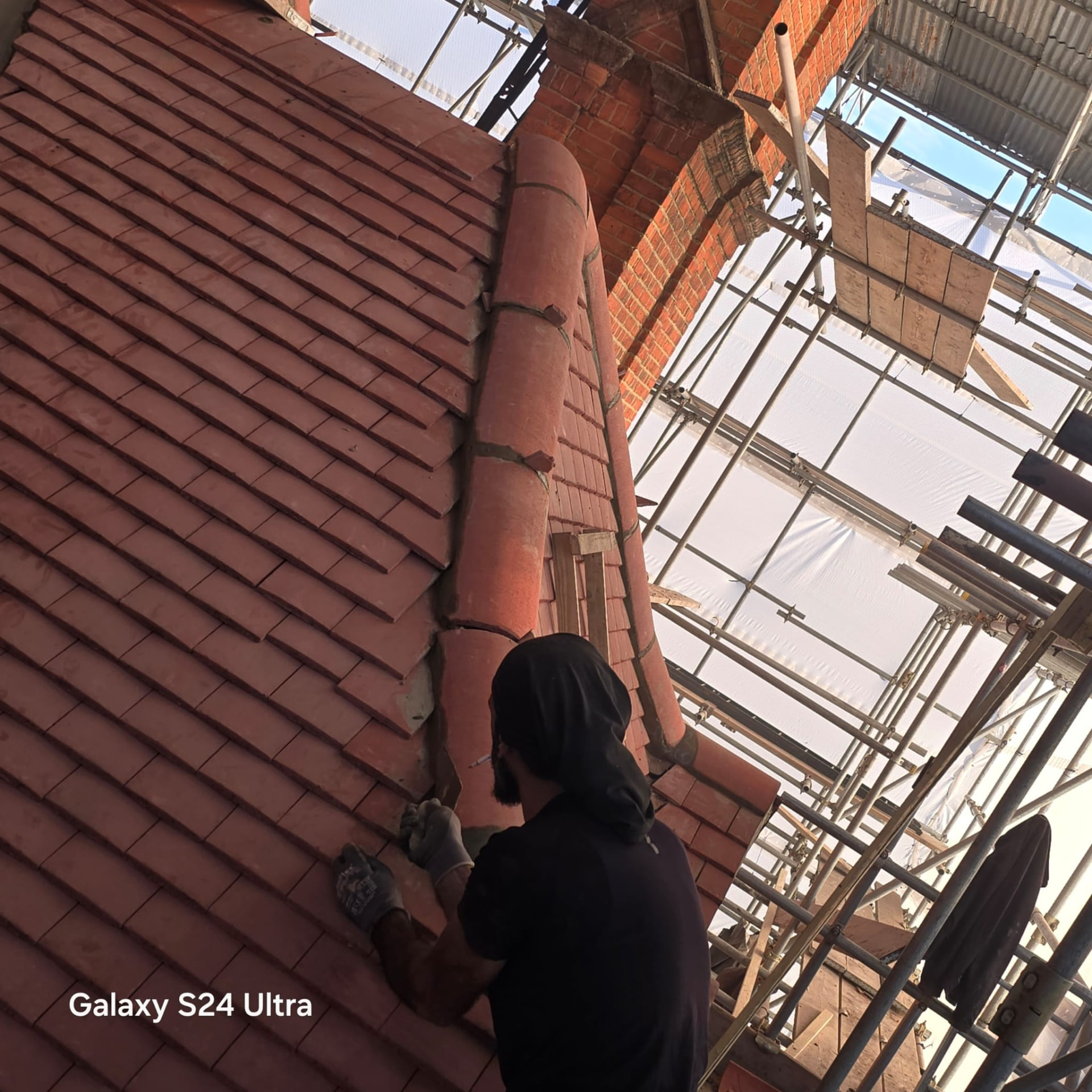 Roofer bedding tiles against the half round hip roll on the newly tiled slope
