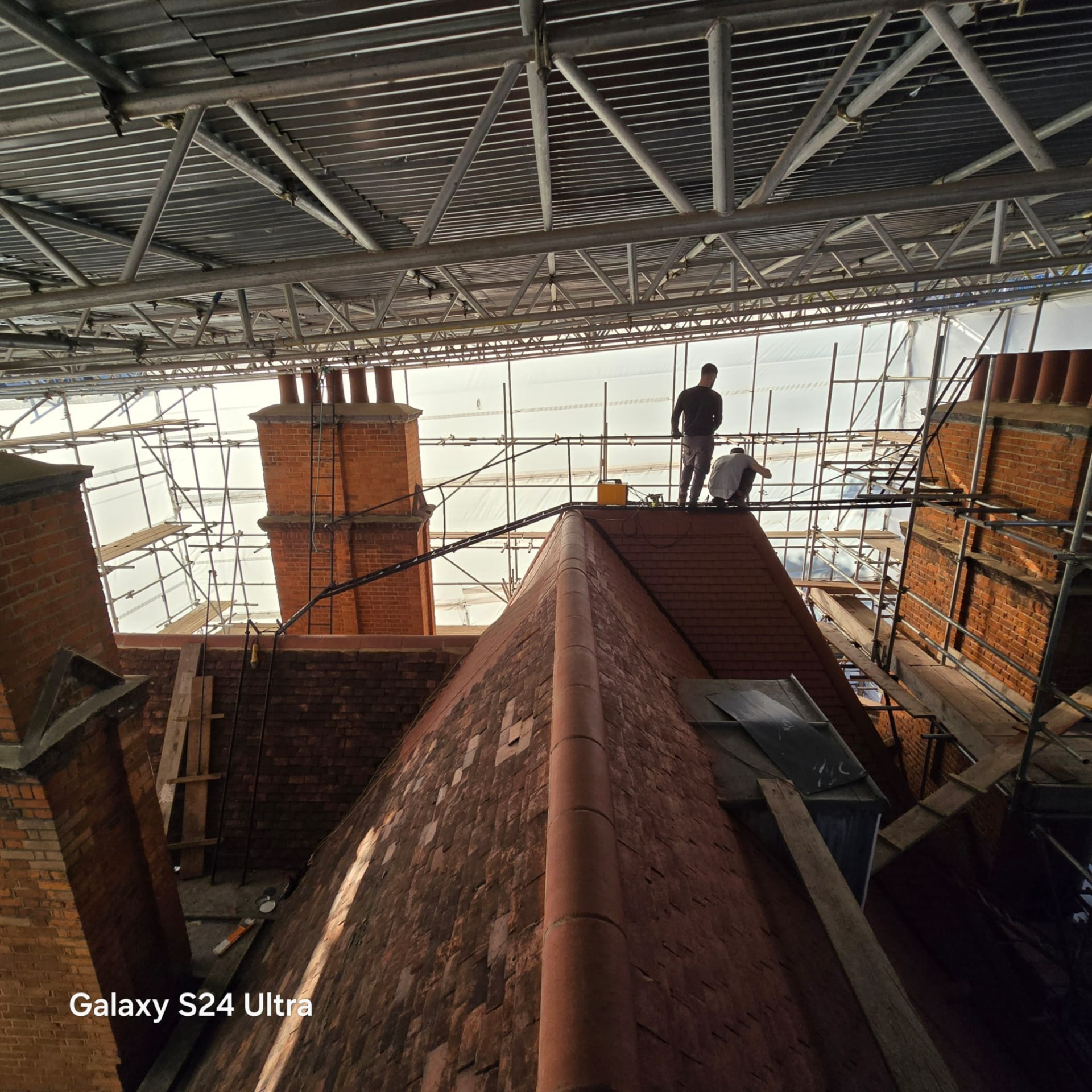 Roofers working along the ridge under the temporary roof, with original chimney stacks either side